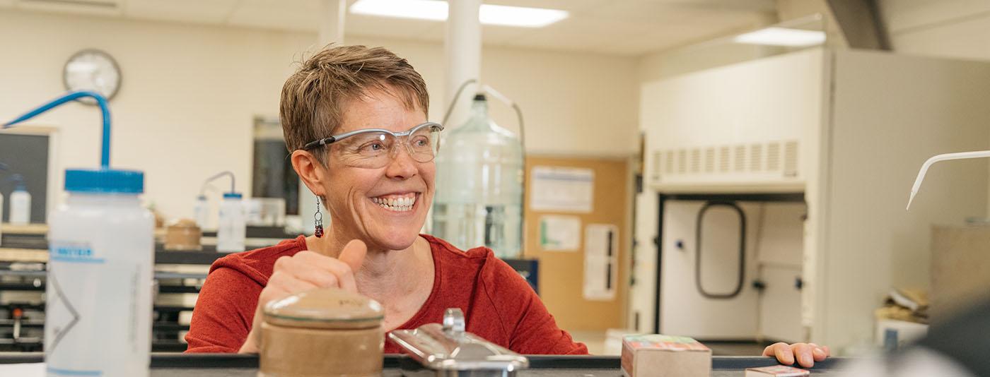 A lab instructor in a red shirt wears safety glasses