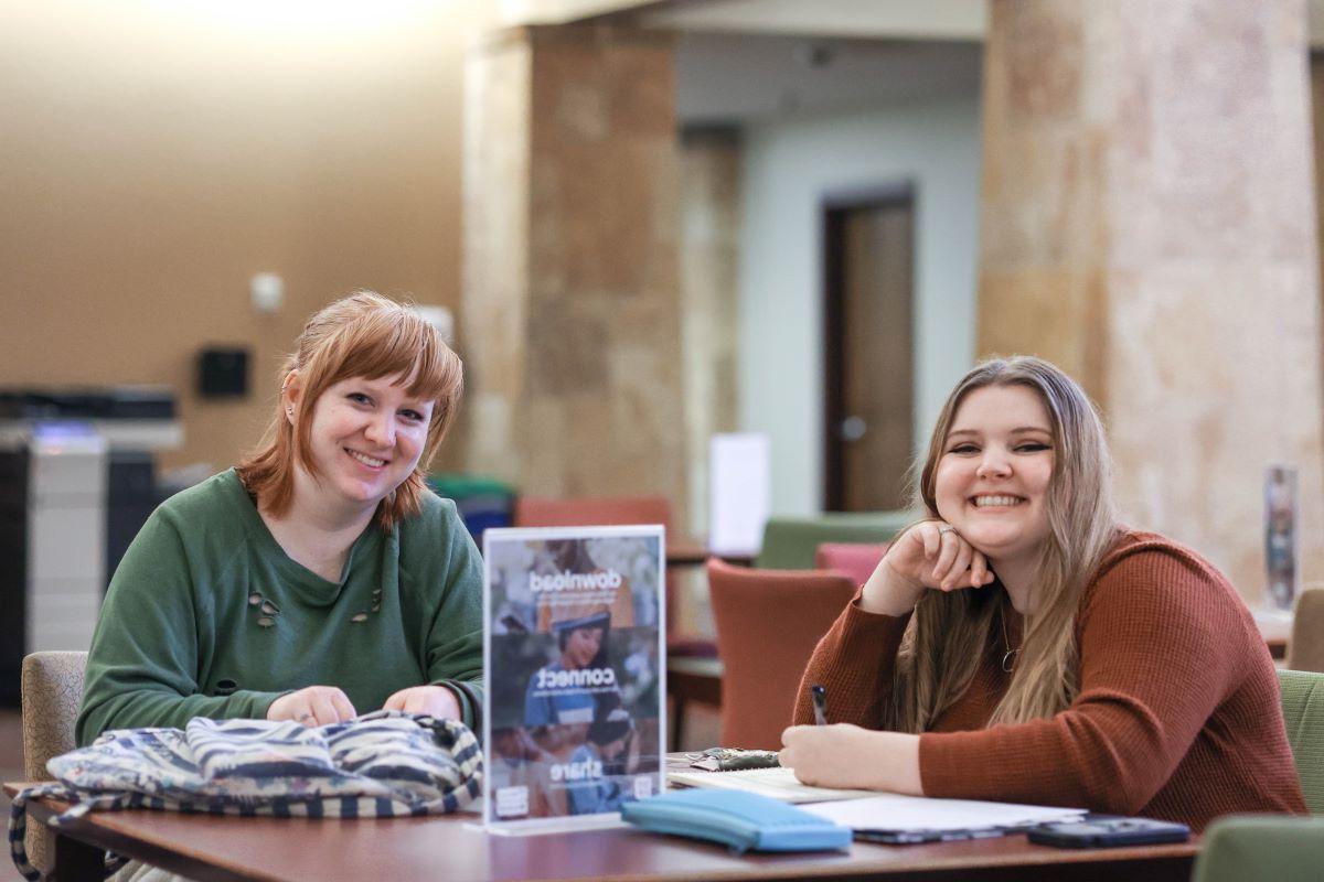 two students at a table smile at the camera